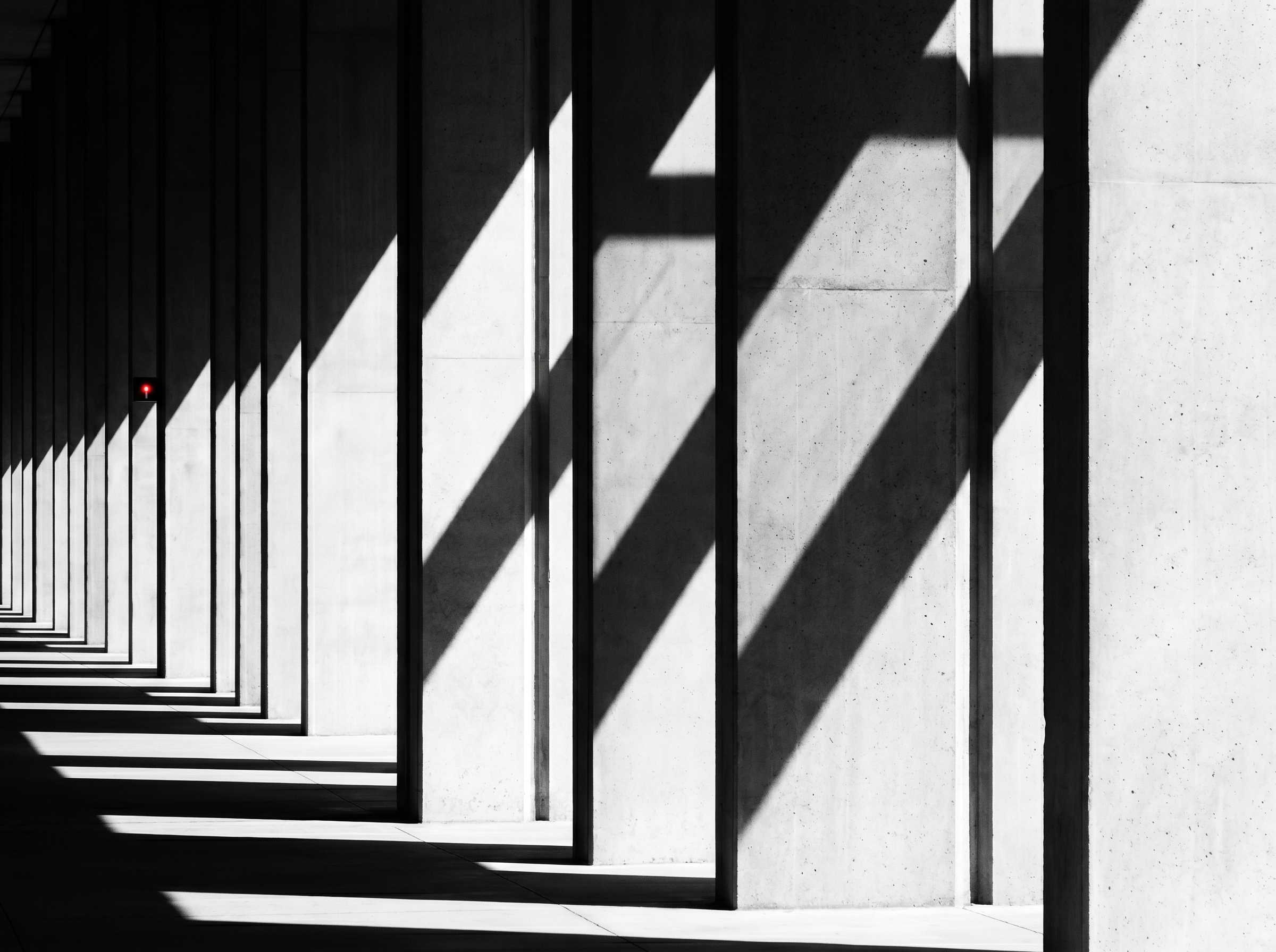 Brutalist corridor of repeating pillars with a single red indicator light