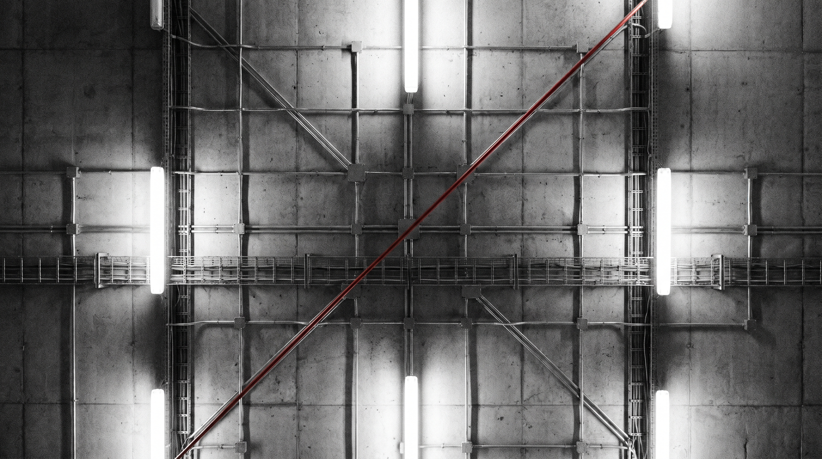 Brutalist concrete ceiling with an industrial grid of conduits and a red cable cutting diagonally through the network